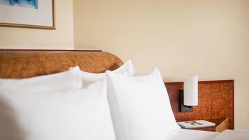 A hotel room with a neatly made bed, a wooden headboard, and a wall-mounted nightstand with a lamp.