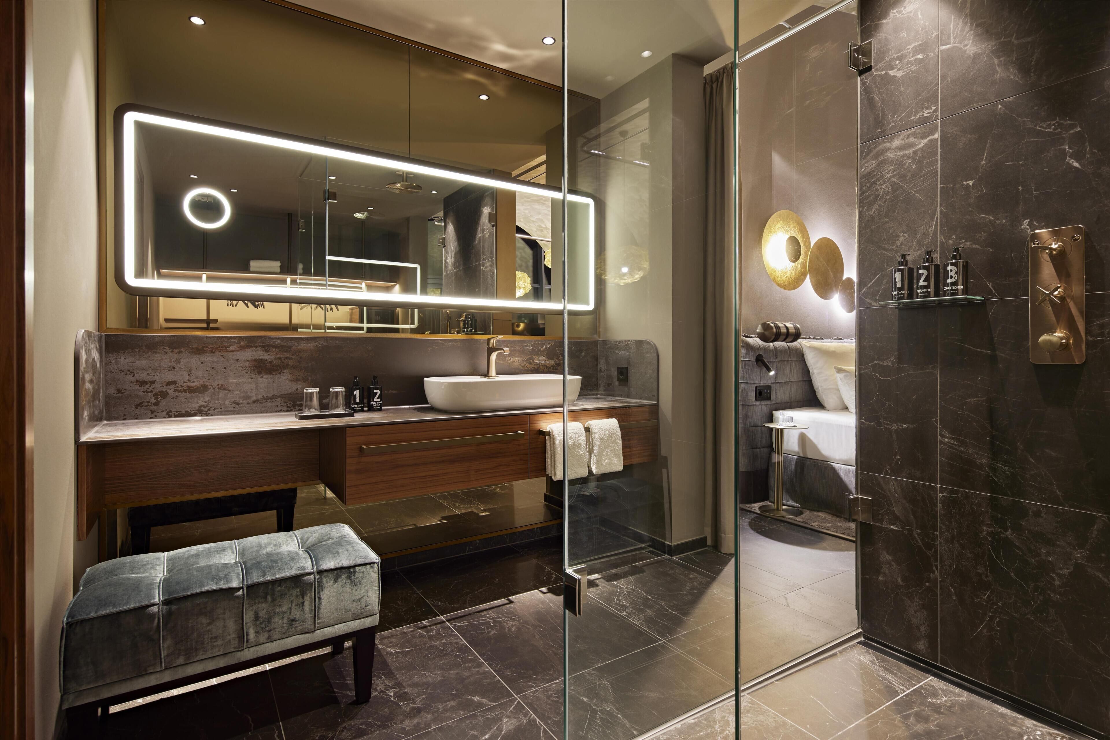 A modern bathroom with a glass-enclosed shower, a vanity with a large mirror, and a bench.