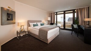 Habitación de hotel con una cama grande, un escritorio, una silla, una lámpara y vistas a la ciudad desde la ventana.
