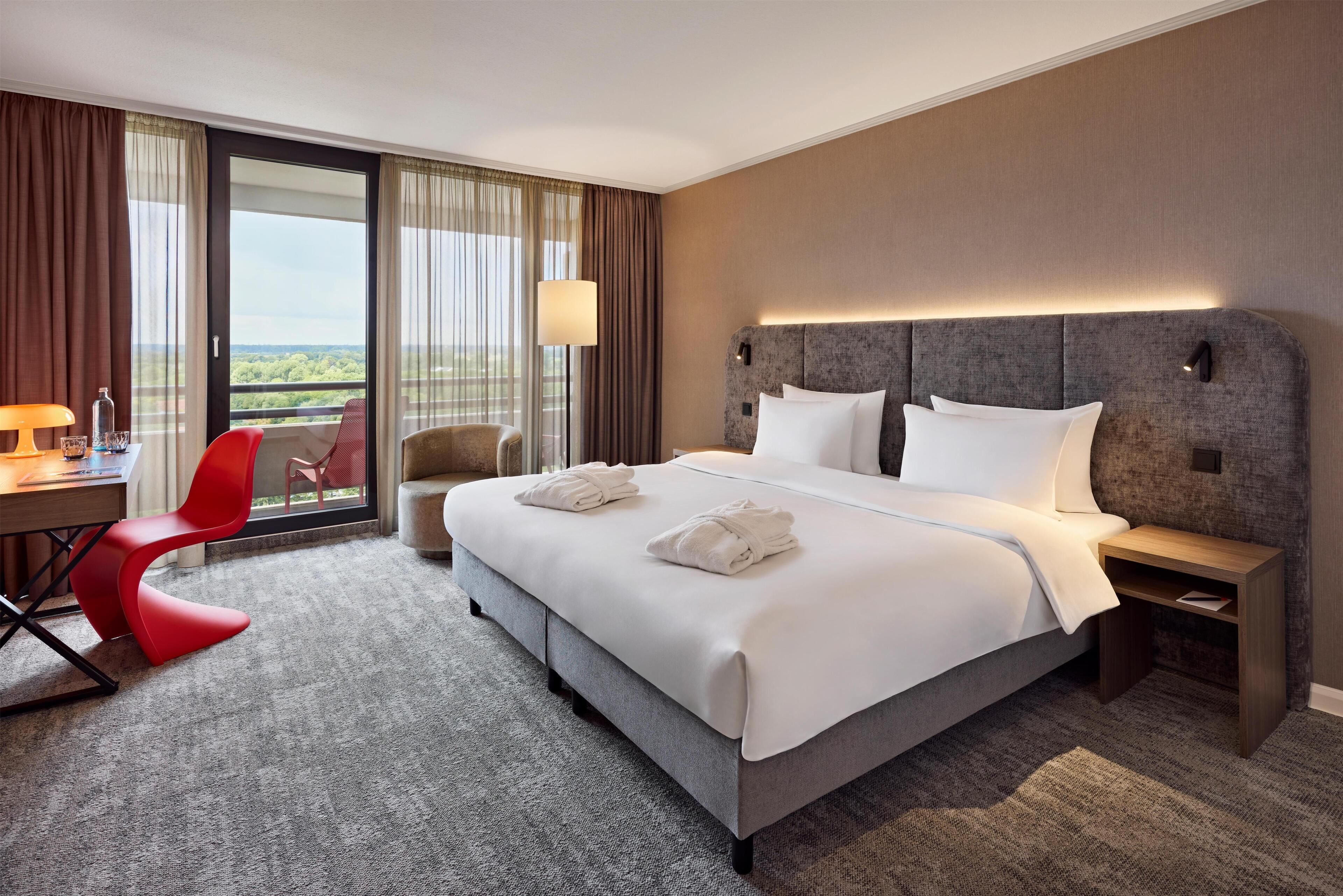 A hotel room with a large bed, a desk with a chair, and a view through the window.