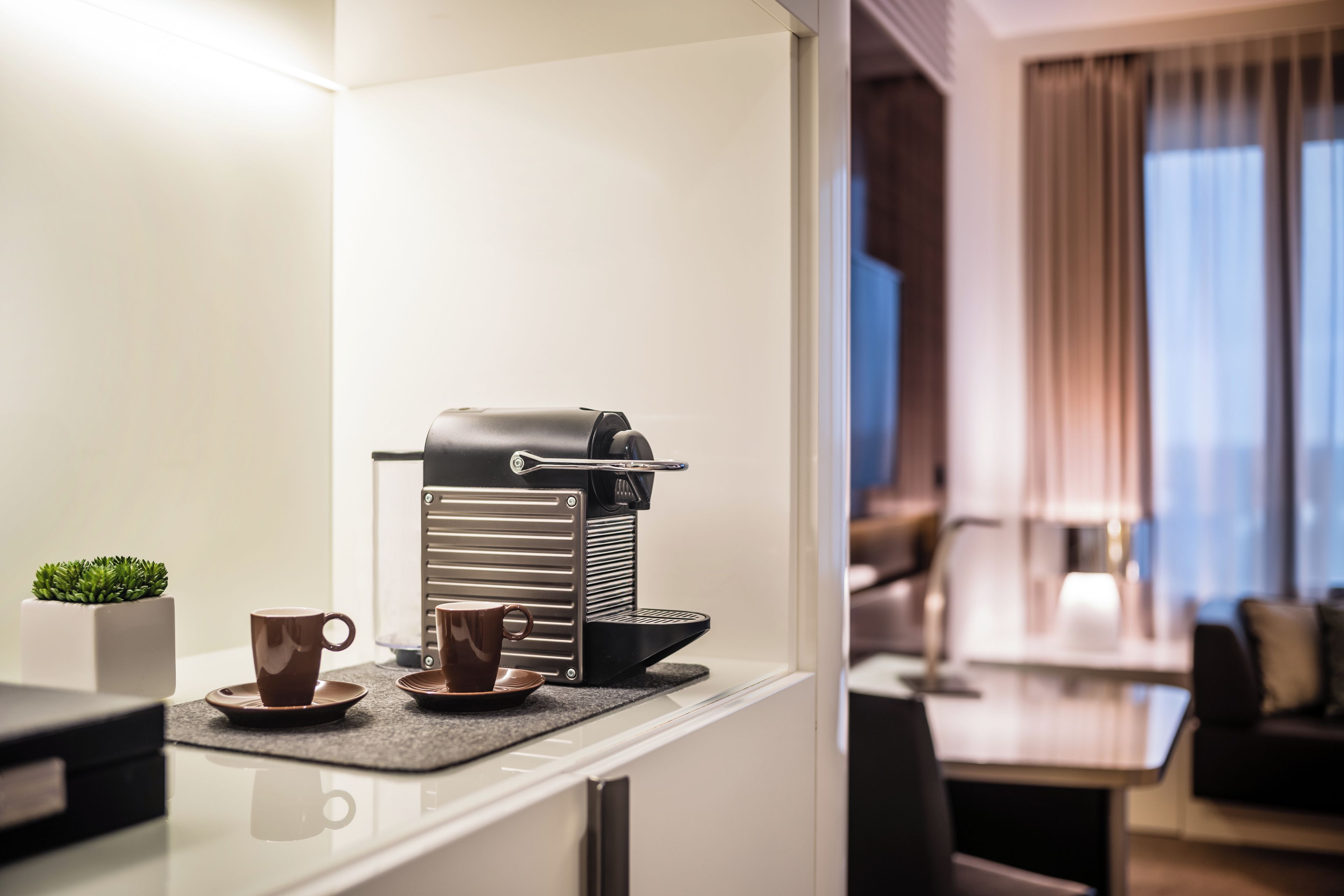 Une cuisine moderne avec une machine à café, deux tasses et une petite plante sur le comptoir.