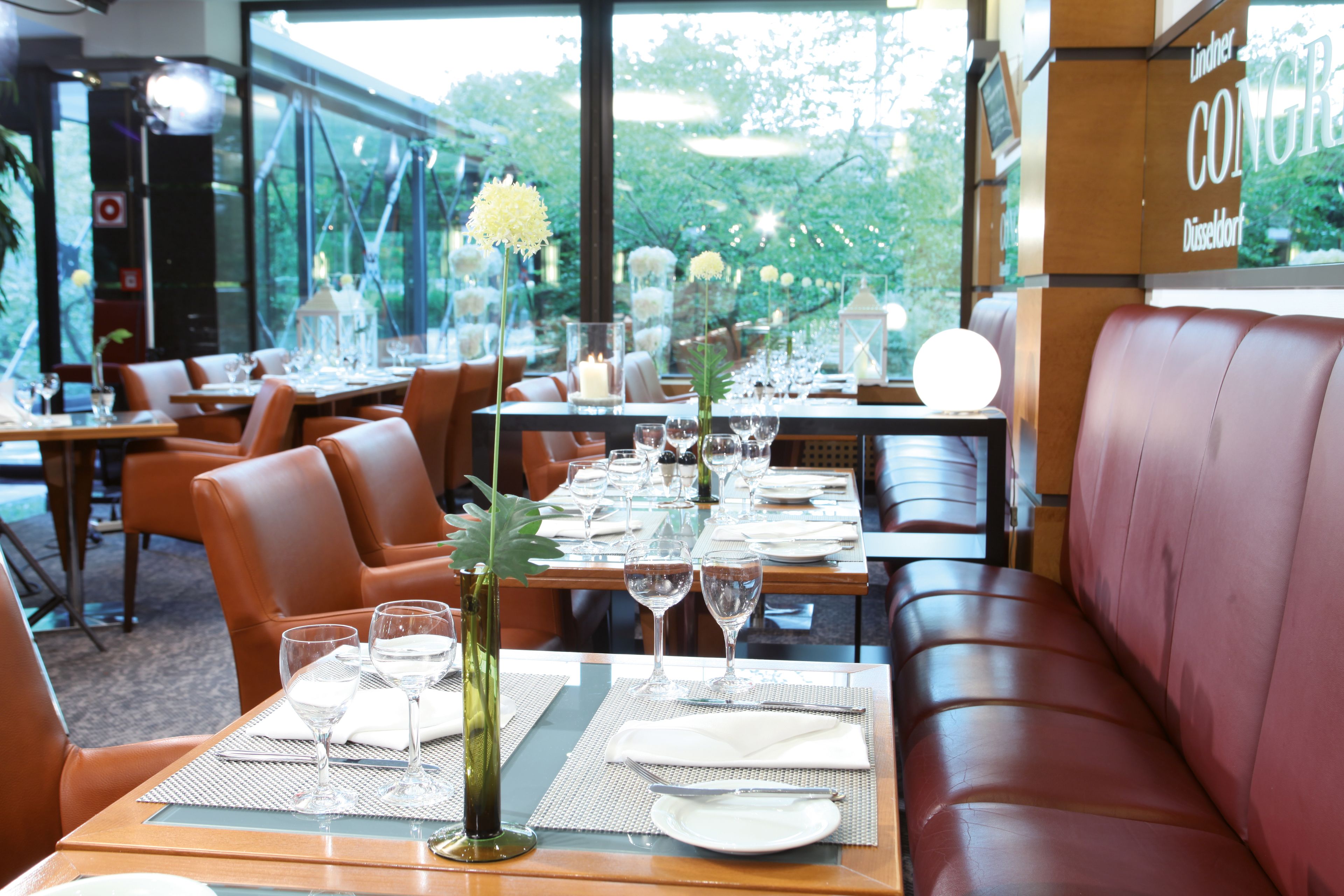 Un restaurant dont les tables sont dressées pour le service, offrant une vue sur la verdure environnante.