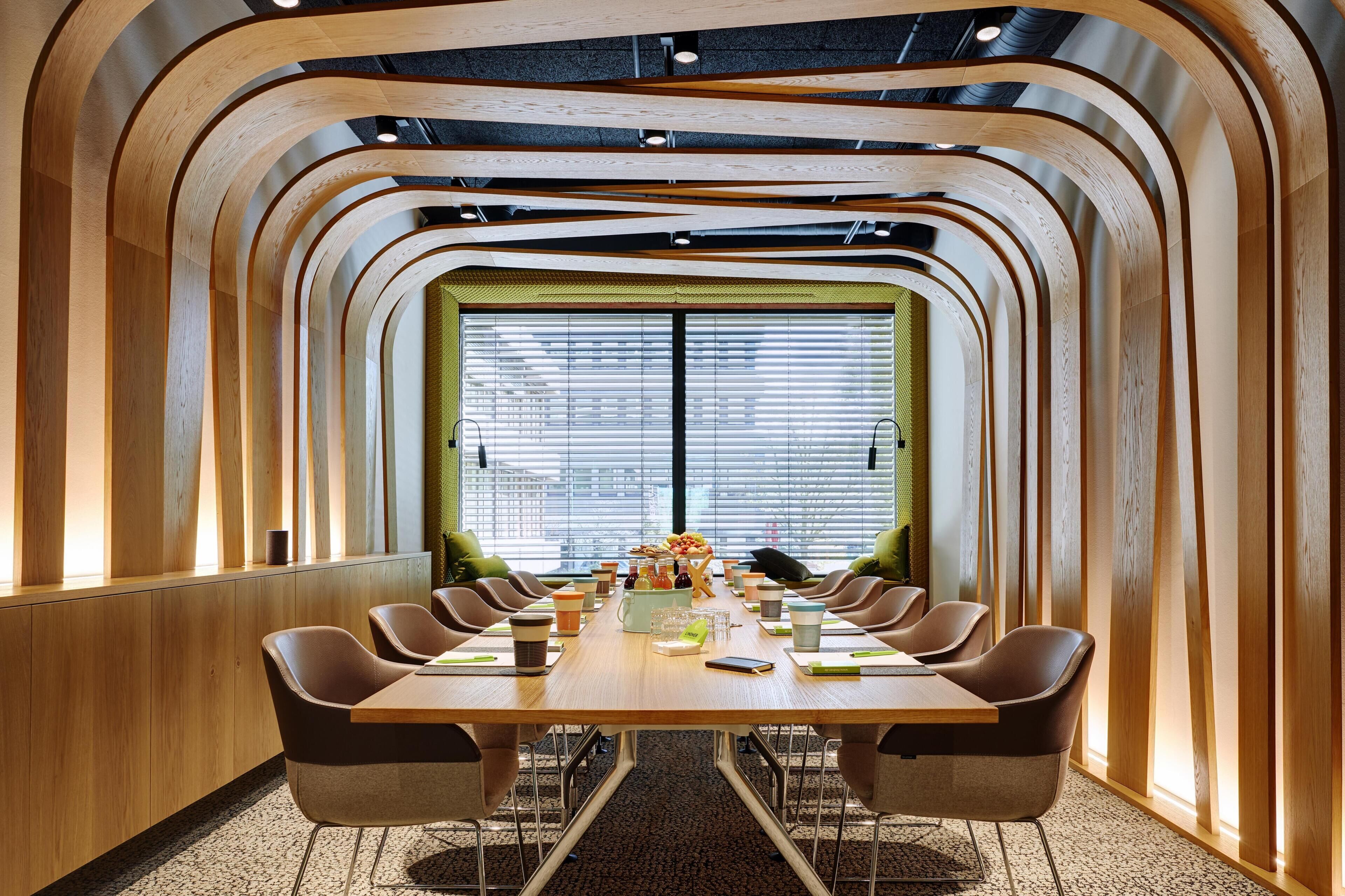 Une salle de conférence avec une longue table, de nombreuses chaises et une grande fenêtre équipée de stores.