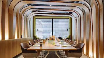 Une salle de conférence avec une longue table, de nombreuses chaises et une grande fenêtre équipée de stores.
