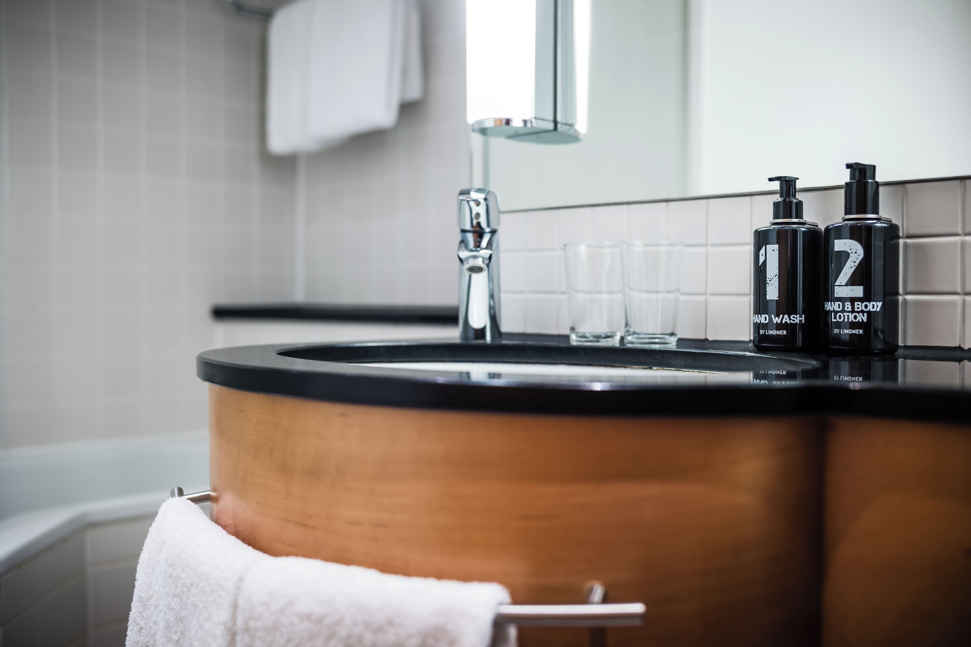 Un baño con un lavabo de madera, dos botellas de crema para manos y cuerpo, y un espejo sobre el lavabo.