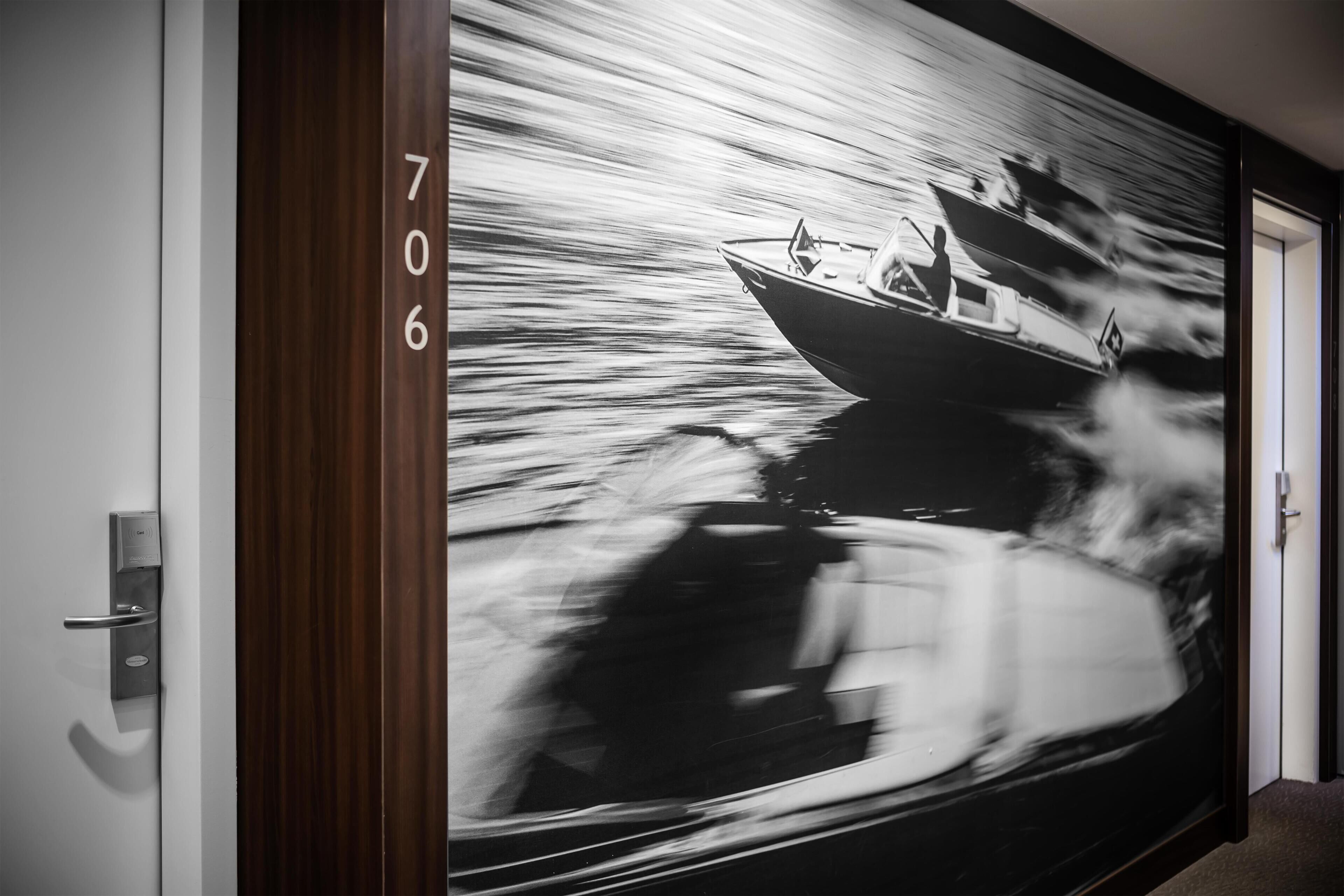 Een gang met een groot muurschildering van een boot op het water, een deur met het nummer '706', en een moderne deurklink.