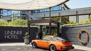 Entrada moderna de un hotel con un Porsche estacionado adelante.