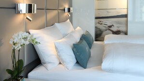 Un dormitorio moderno con cama, ropa de cama blanca, una orquídea en maceta y un aplique de pared.