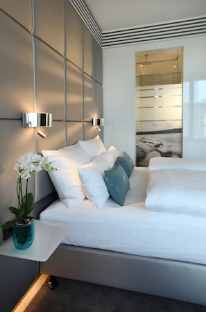 A modern bedroom with a bed, white bedding, a potted orchid, and a wall-mounted light fixture. - Lindner Dusseldorf Seestern, Part of JdV by Hyatt (Düsseldorf)