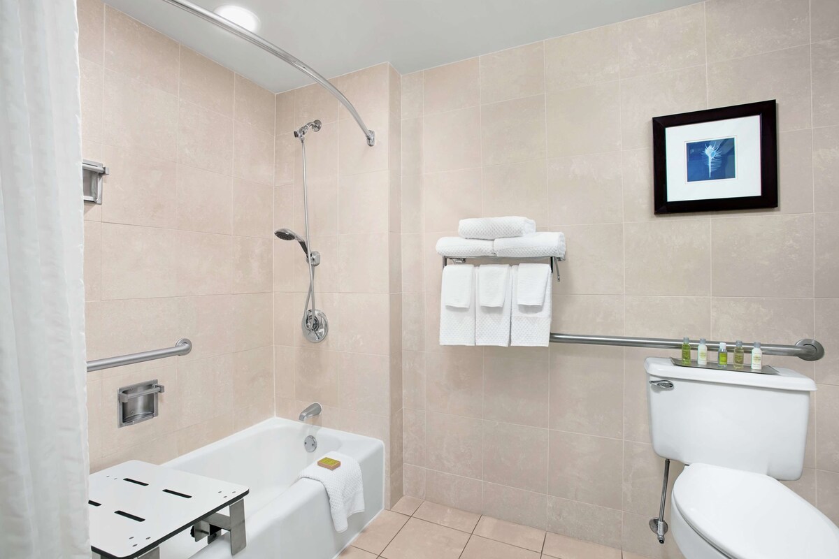 A modern bathroom with a bathtub, shower, and toilet. There are towels and toiletries on the wall.