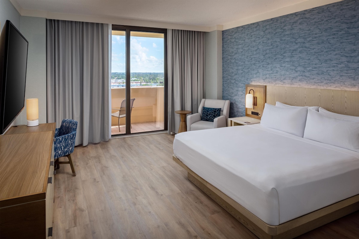 A hotel room with a large bed, a desk, a chair, a small table, and a TV.