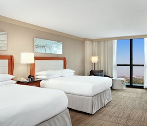 A hotel room with two beds, a desk, a lamp, a phone, and a view of the city through large windows. - DoubleTree by Hilton Hotel Miami Airport & Convention Center (Miami)
