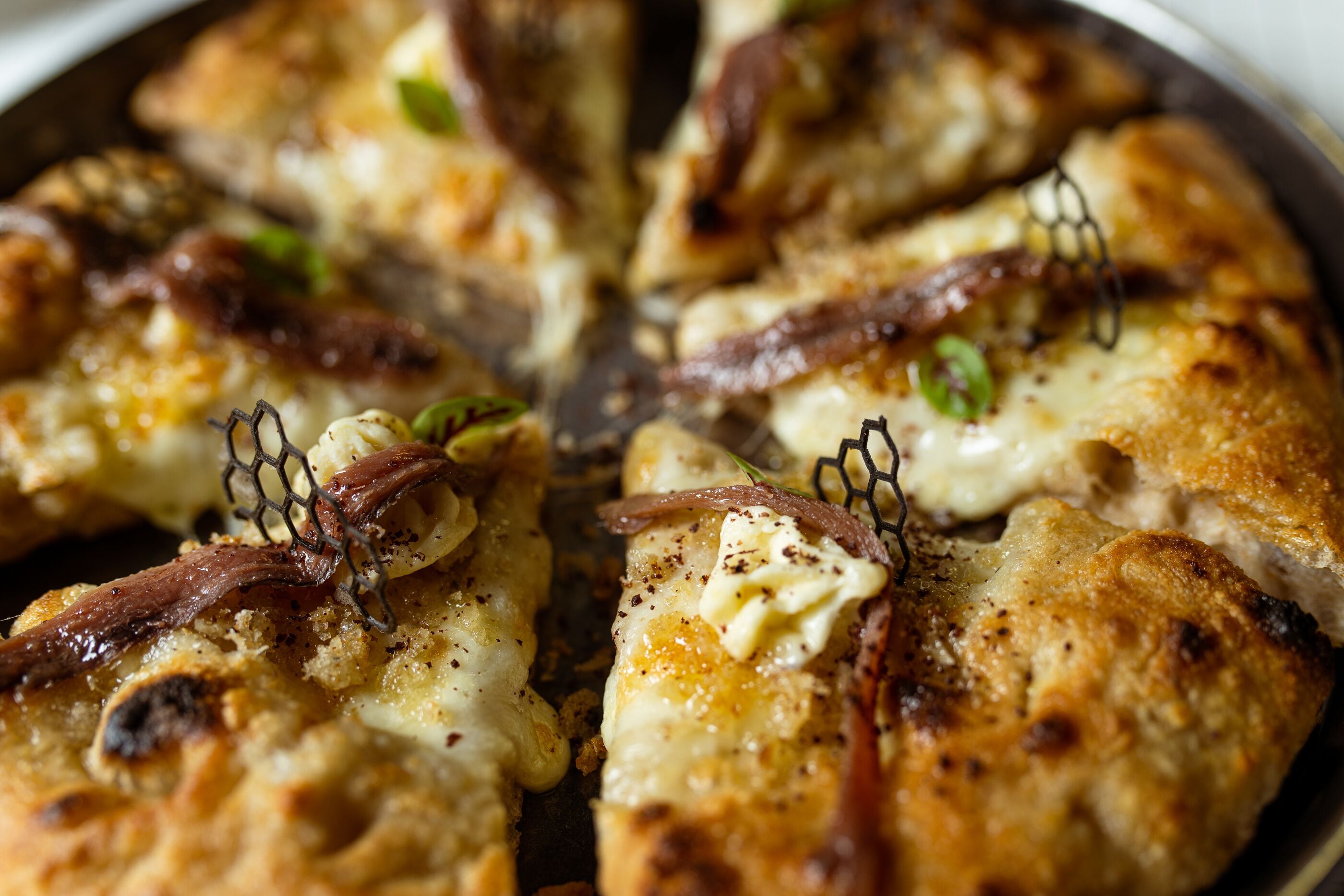 A close-up of a pizza with cheese, herbs, and bacon on a pan.