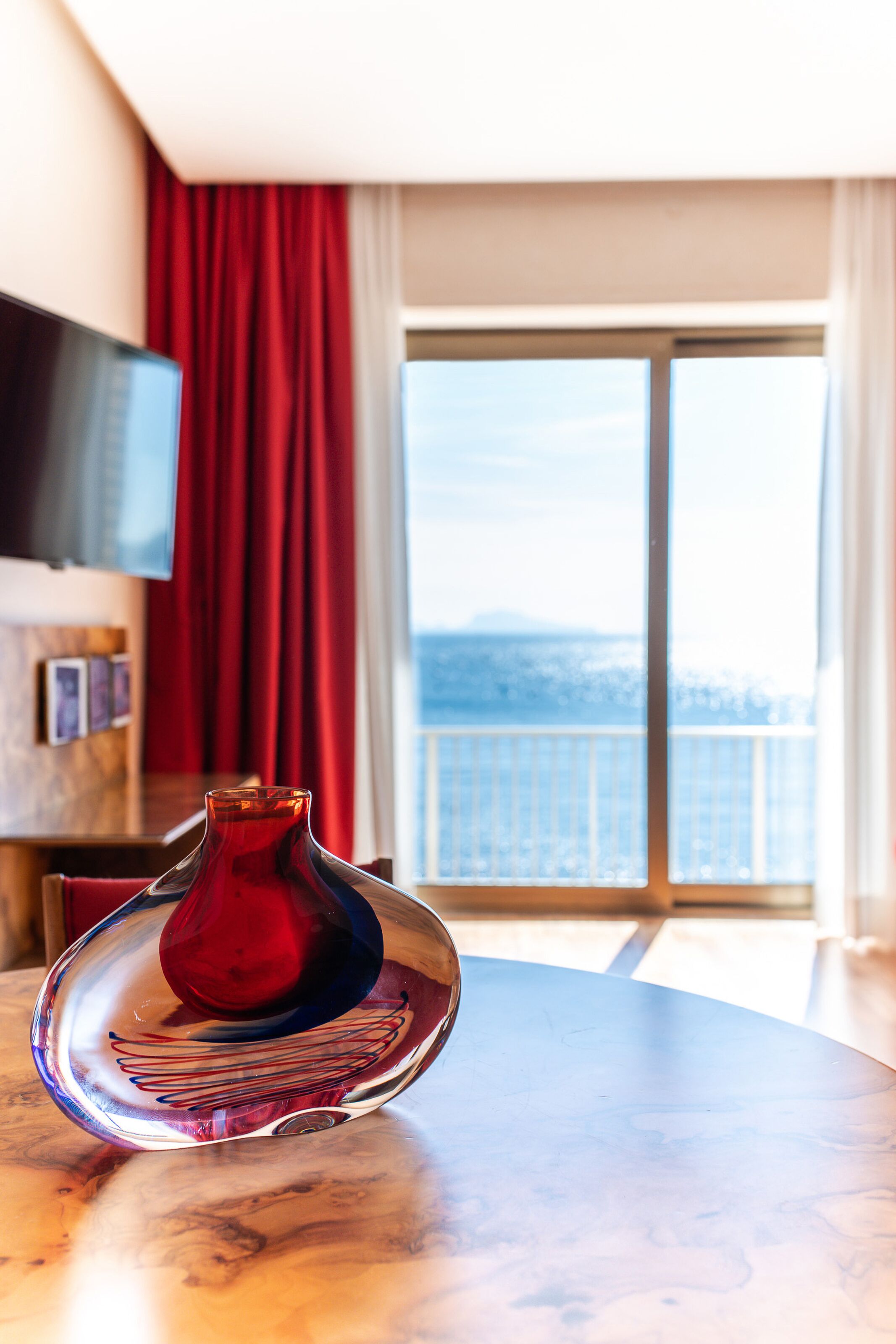 Ein Zimmer mit einem runden Tisch, einer roten Vase und Meerblick vom Balkon.