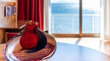 Una stanza con un tavolo rotondo, un vaso rosso e vista mare da un balcone.