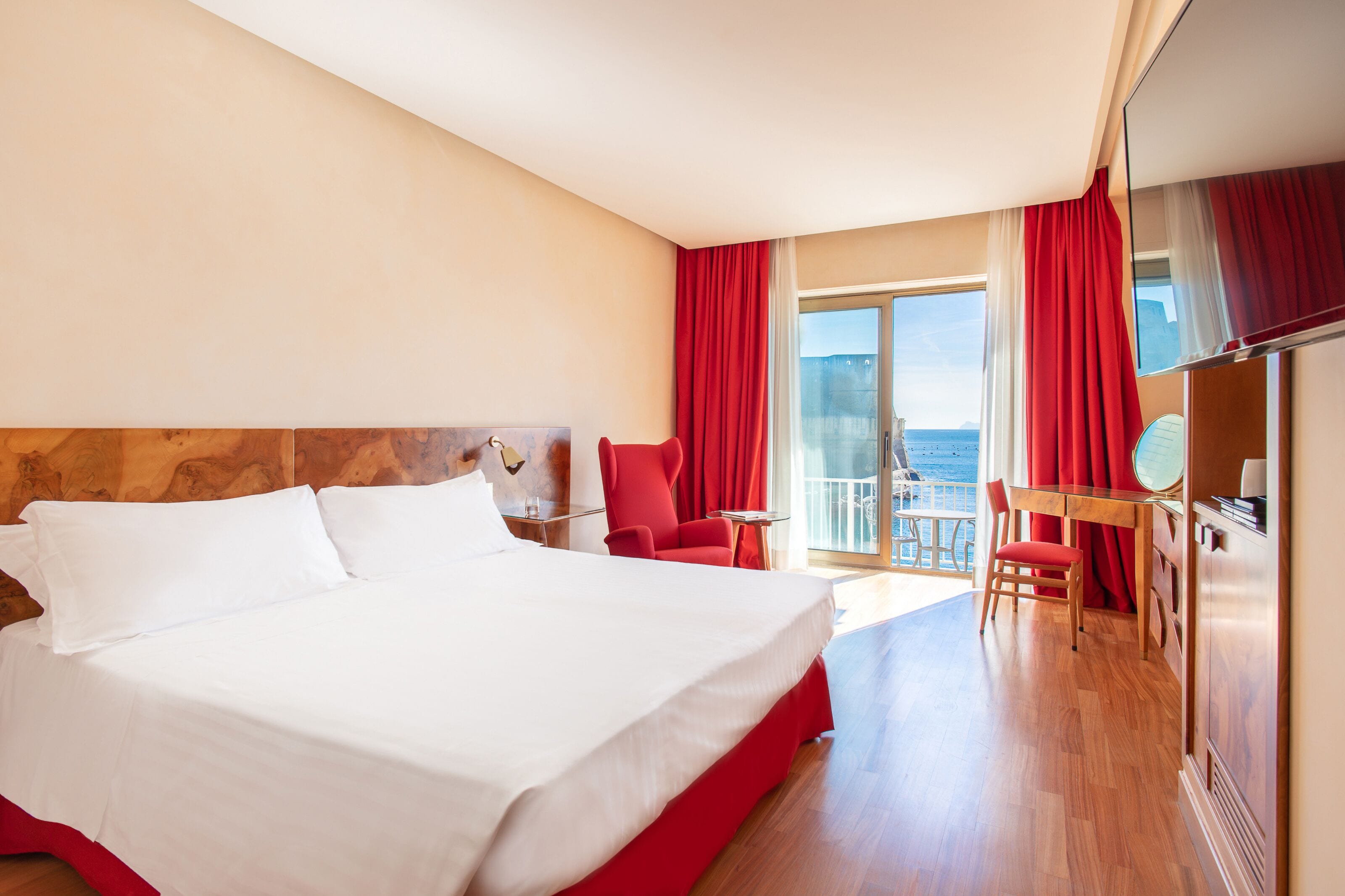 Habitación de hotel con una cama grande, un escritorio con silla y vistas al mar desde el balcón.
