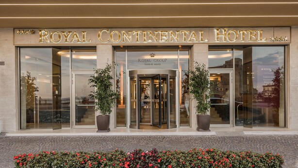 The exterior of the Royal Continental Hotel with a prominent entrance, large glass doors, and potted plants. - Royal Continental Hotel Naples (Naples)