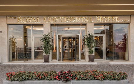 The exterior of the Royal Continental Hotel with a prominent entrance, large glass doors, and potted plants.