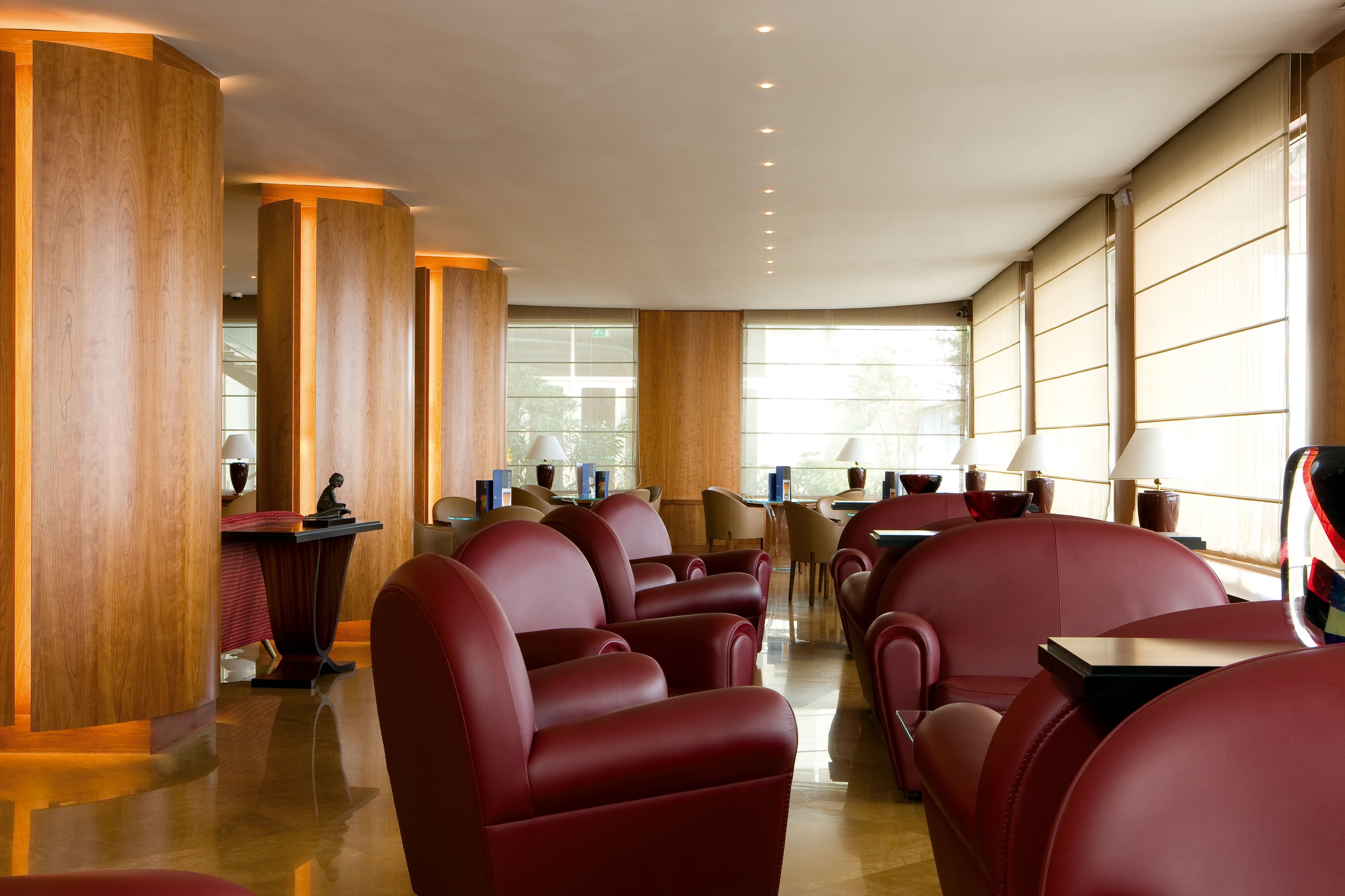A modern hotel lobby with red leather seating, wooden pillars, and large windows providing natural light.