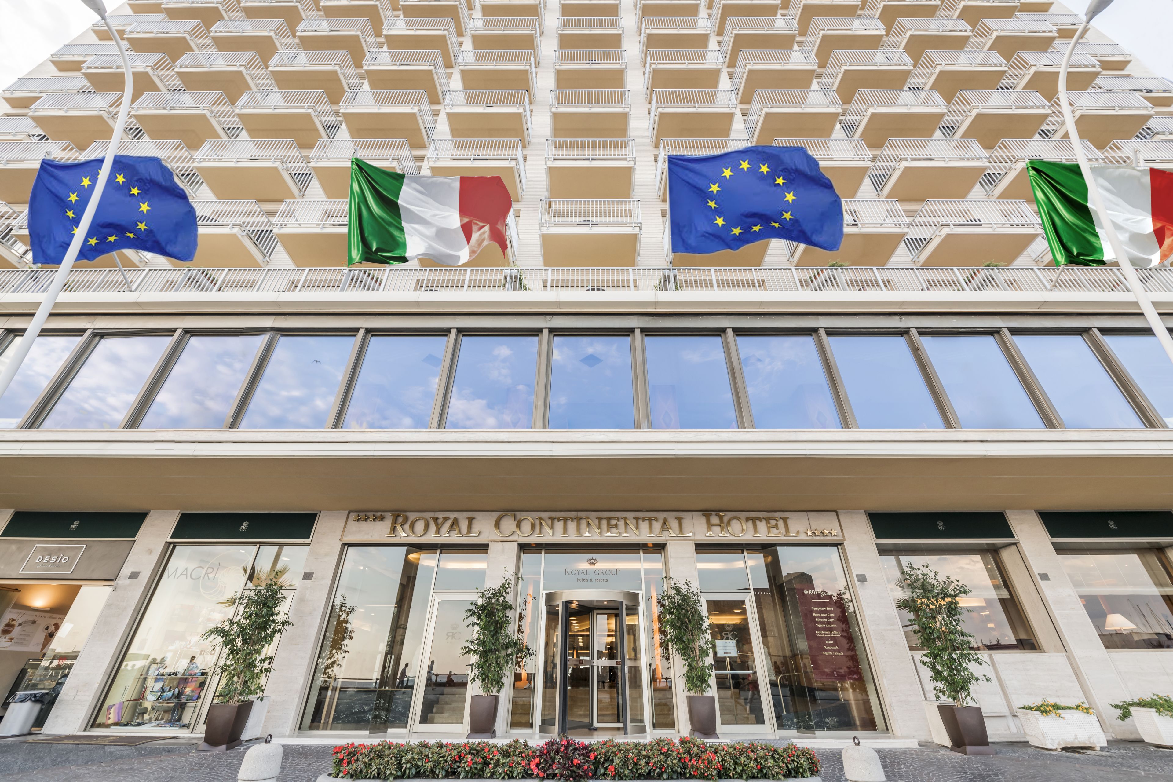 La façade de l’hôtel Royal Continental, ornée de nombreux drapeaux, dont le drapeau de l’Union européenne, offre une vue dégagée sur l’entrée.