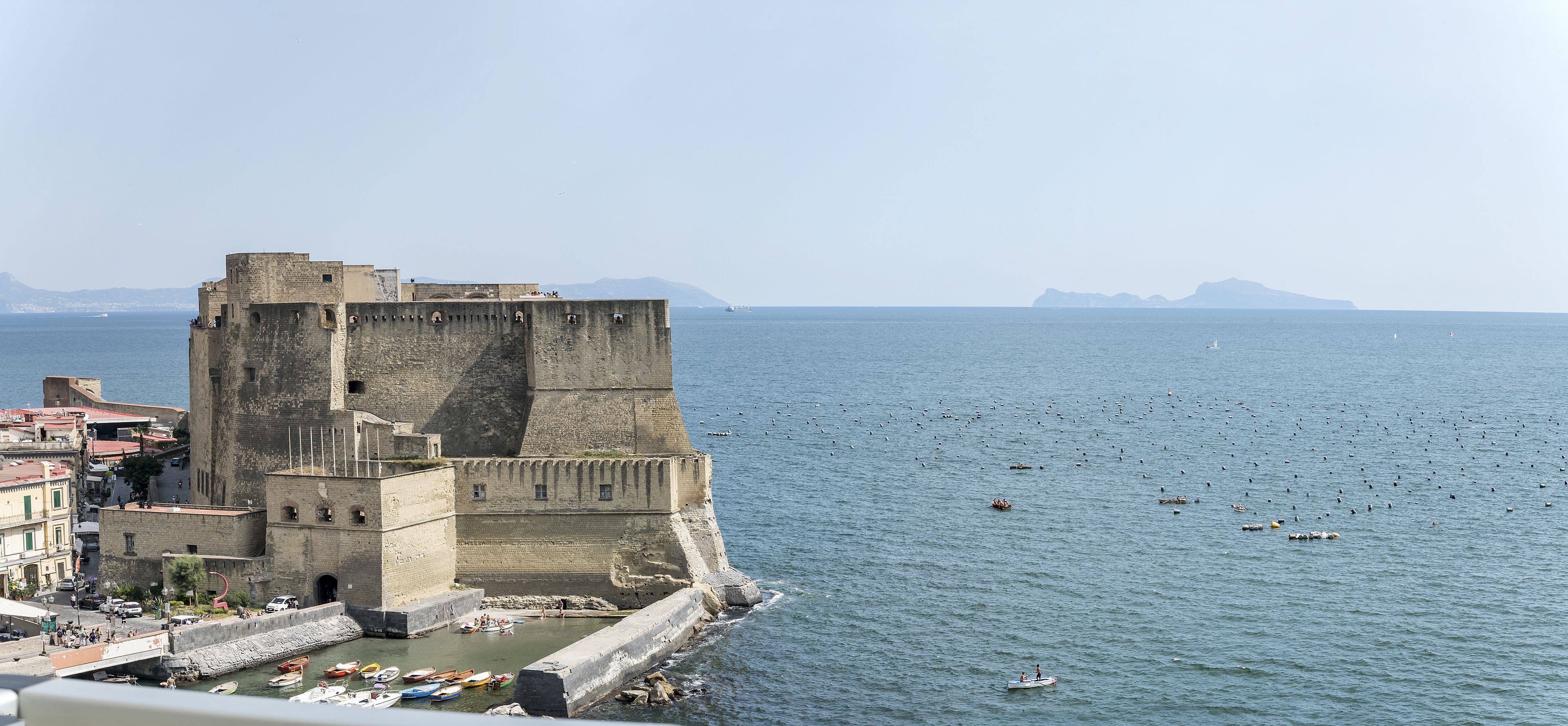 Una fortaleza de piedra histórica junto al mar, con vistas a barcos y un cielo despejado.