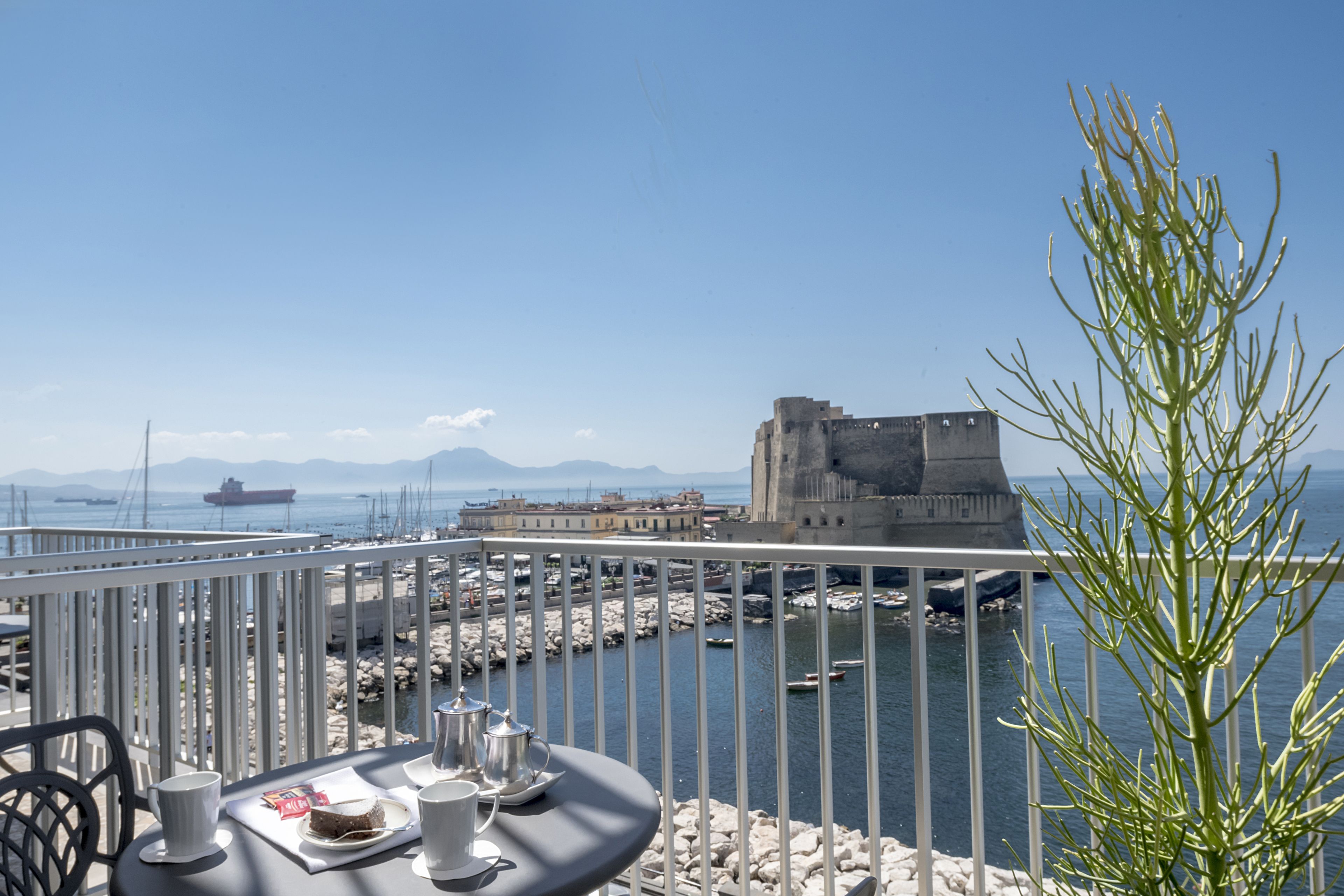 A balcony with a table set for two, overlooking a marina with boats and a historic building.