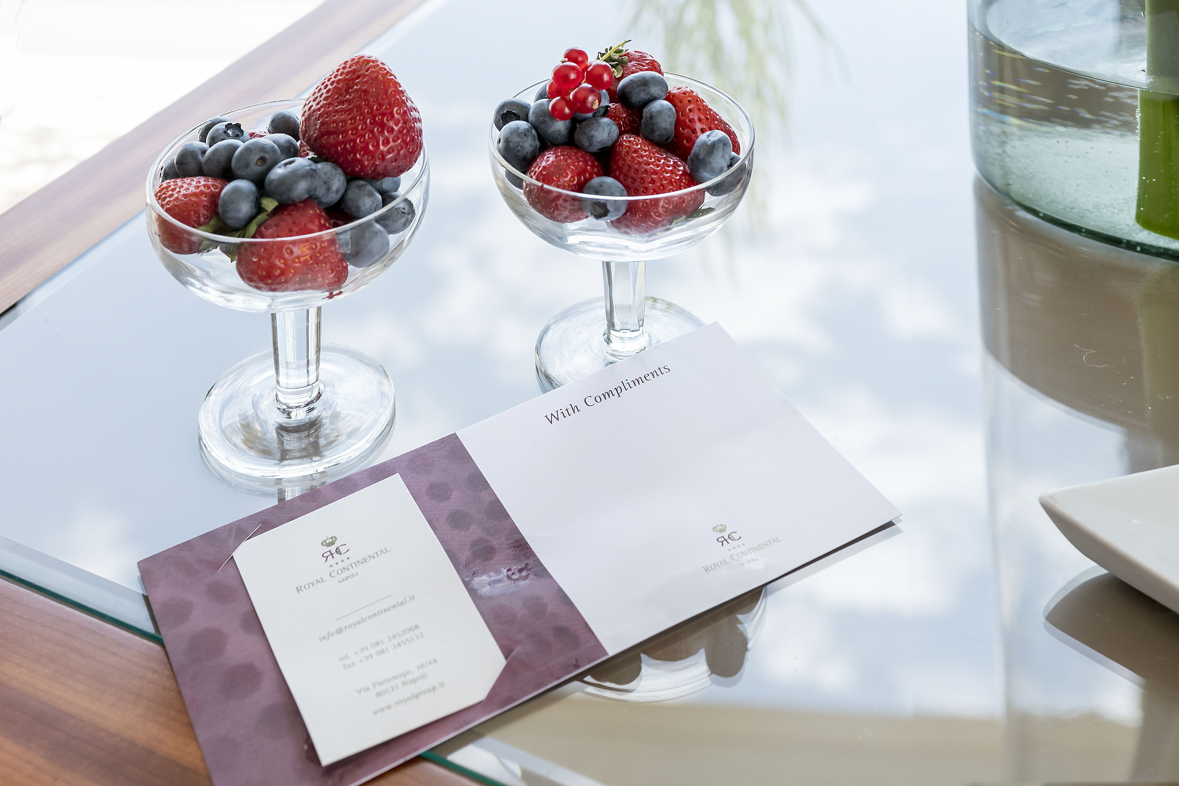 To skåle med dessert på et glasbord, sammen med et visitkort og en lilla konvolut.