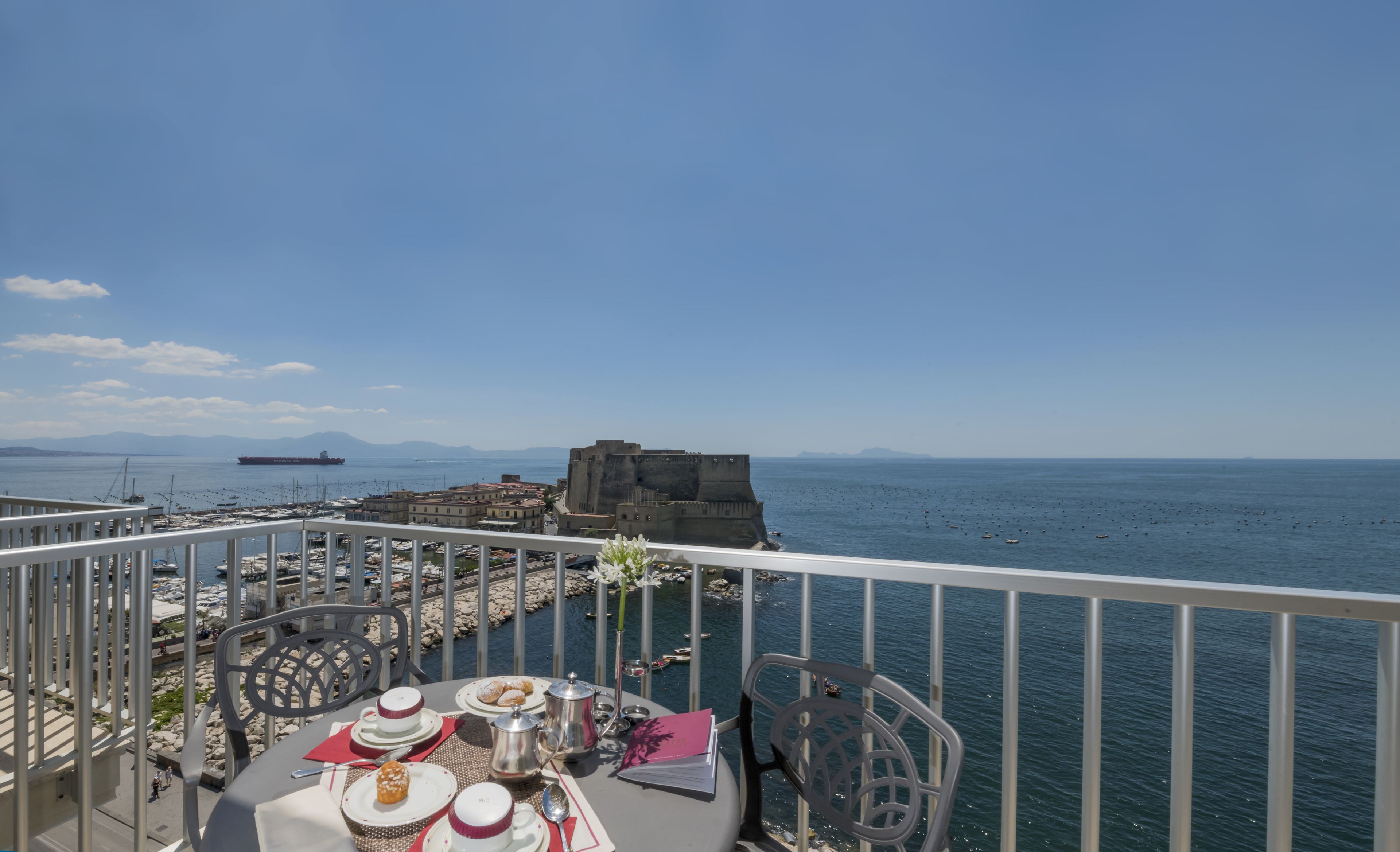 A table set with tea service and pastries, overlooking a marina and a historic fort.