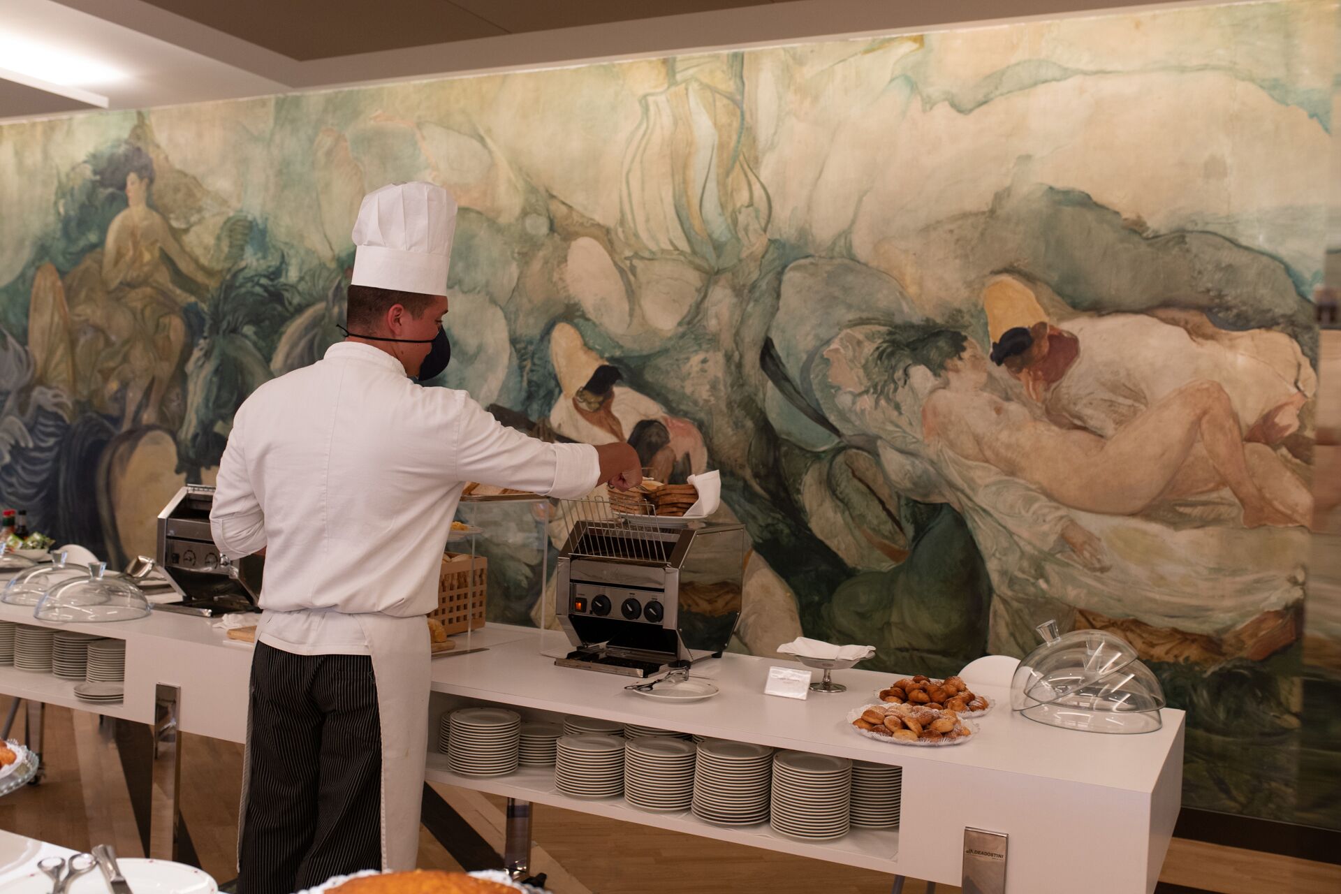 Uno chef prepara il cibo a un buffet con un grande quadro astratto sullo sfondo.