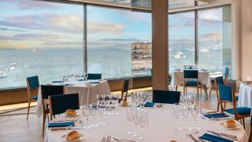 A dining area with tables set for a meal, overlooking a body of water with boats.