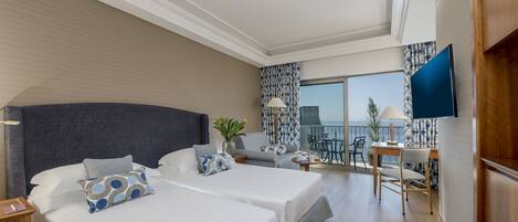 A hotel room with two beds, a desk, a chair, a TV, and a balcony with a view.