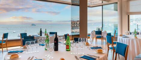A restaurant with round tables set for dining, overlooking a body of water with boats.