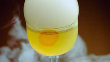 Um cocktail num copo com esquema de cores branco e amarelo, em frente a um fundo desfocado.