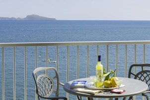 Un balcon avec une table dressée pour deux personnes, agrémentée d’une bouteille de limoncello, de citrons et d’un menu.