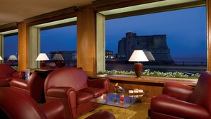 A hotel room with leather sofas, a glass coffee table, and a view of a castle. - Royal Continental Hotel Naples (Naples)