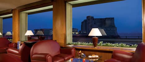 Une chambre d’hôtel avec des canapés en cuir, une table basse en verre et une vue sur un château.