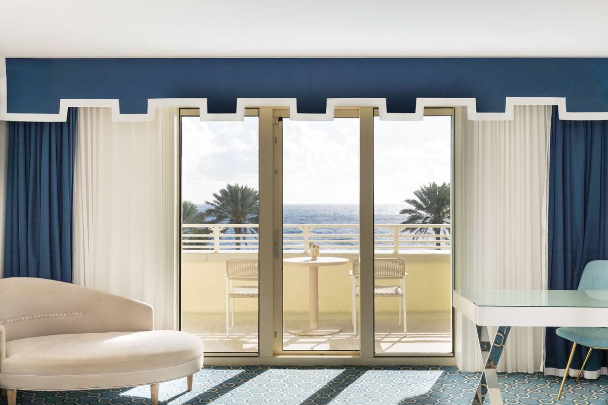 Een kamer met uitzicht op zee, een balkon met stoelen, een tafel en een bank.