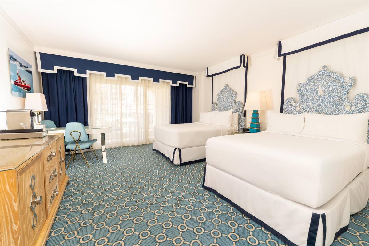 Een hotelkamer met een groot bed, twee kleinere bedden, een bureau, een stoel en een dressoir.