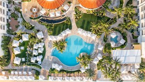 An aerial view of a resort with a central swimming pool, lounge areas, and palm trees. - Eau Resort & Spa (Manalapan)