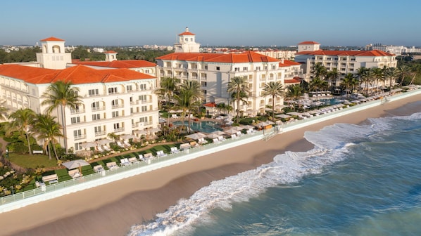 Ein Strandhotel mit mehreren Gebäuden, einem Schwimmbad und einem Strand mit Sonnenschirmen.
