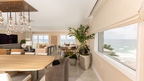 A spacious living area with a large wooden dining table, comfortable seating, and a view of the ocean. - Eau Resort & Spa (Manalapan)