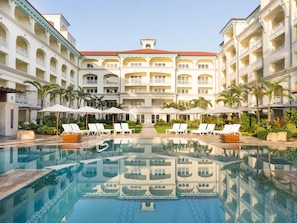 Ein Hotel mit zentralem Pool, mehreren Balkonen und Liegestühlen.