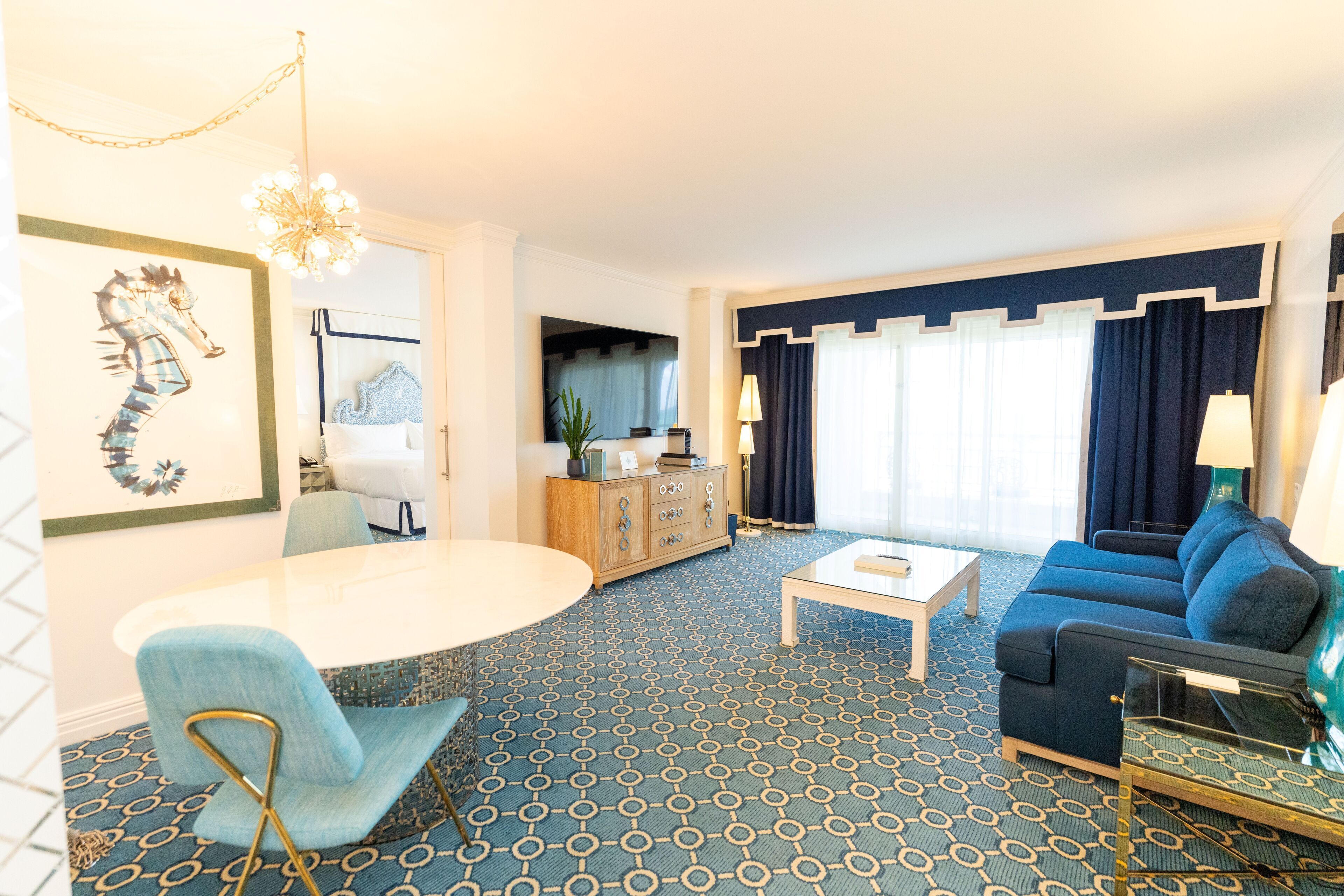 Una sala de estar con alfombra azul estampada, sofá azul, una mesita de centro blanca, sillón azul y un candelabro.