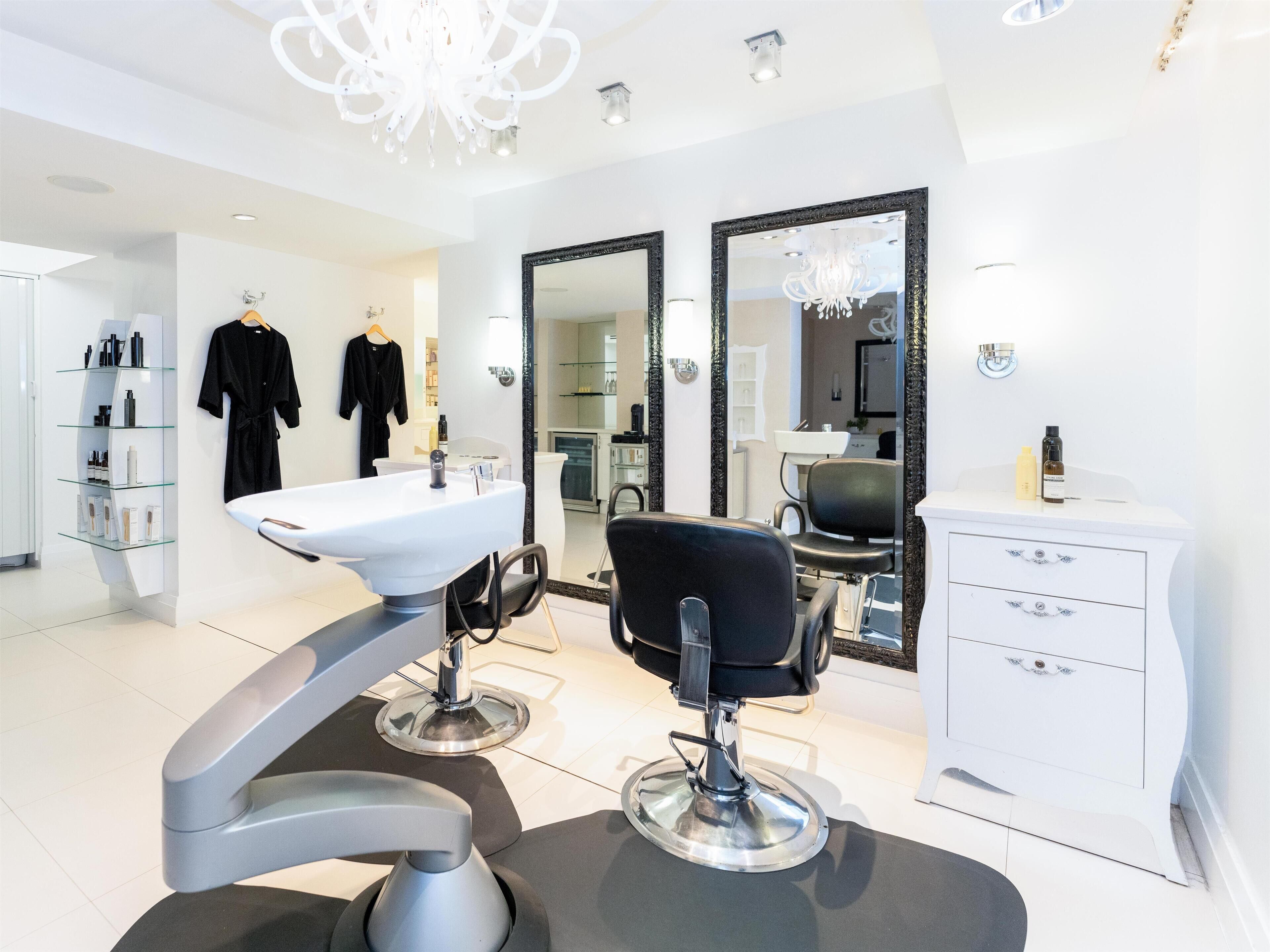 A modern salon with a white sink, black salon chair, and a large mirror.