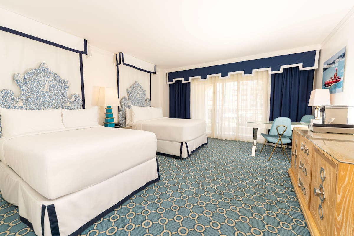 Een hotelkamer met een groot bed, een kleiner bed, een bureau, een stoel en een dressoir.