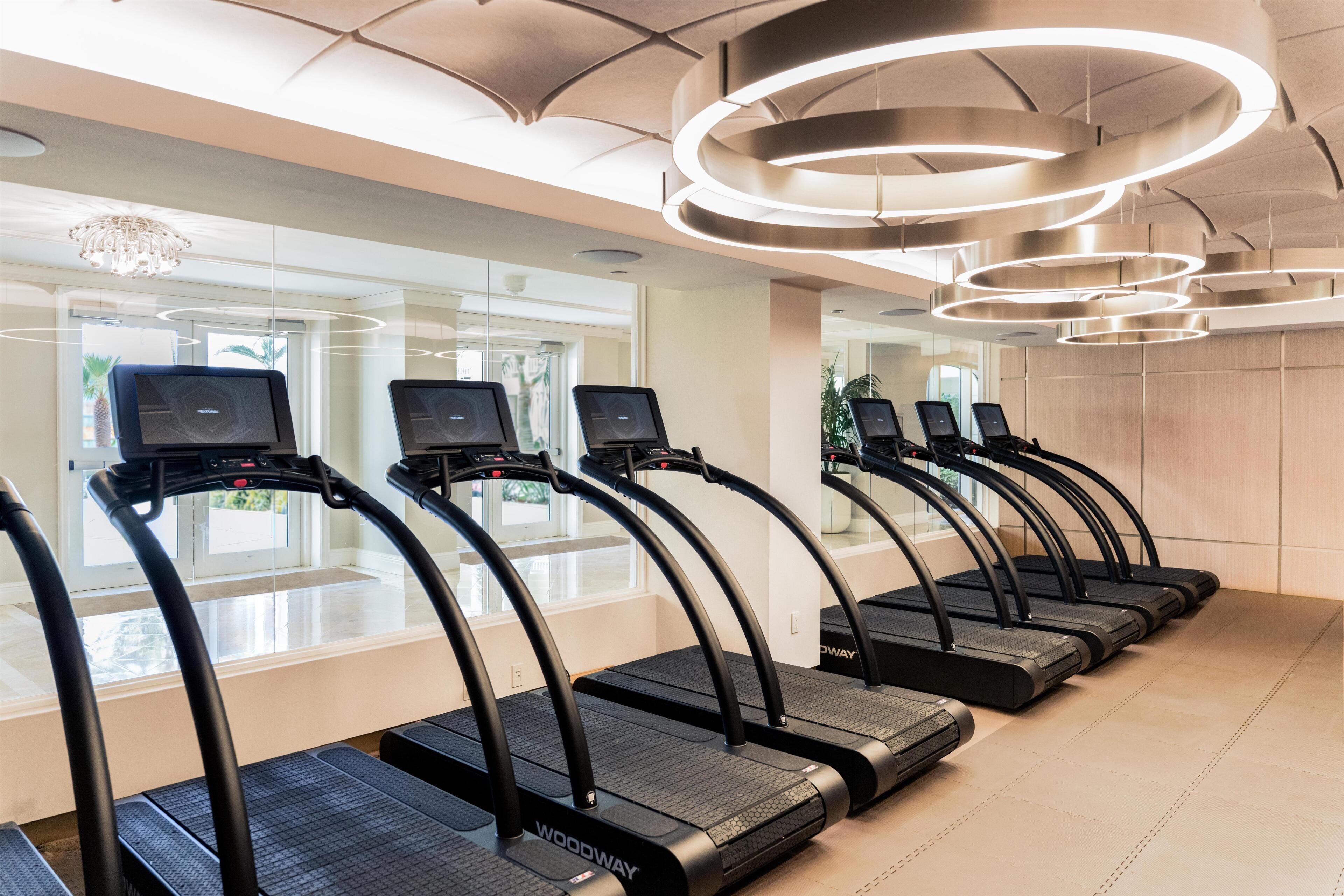 Una hilera de cintas de correr en una sala bien iluminada con un diseño moderno del techo y ventanas amplias.