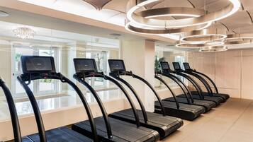 Una hilera de cintas de correr en una sala bien iluminada con un diseño moderno del techo y ventanas amplias.