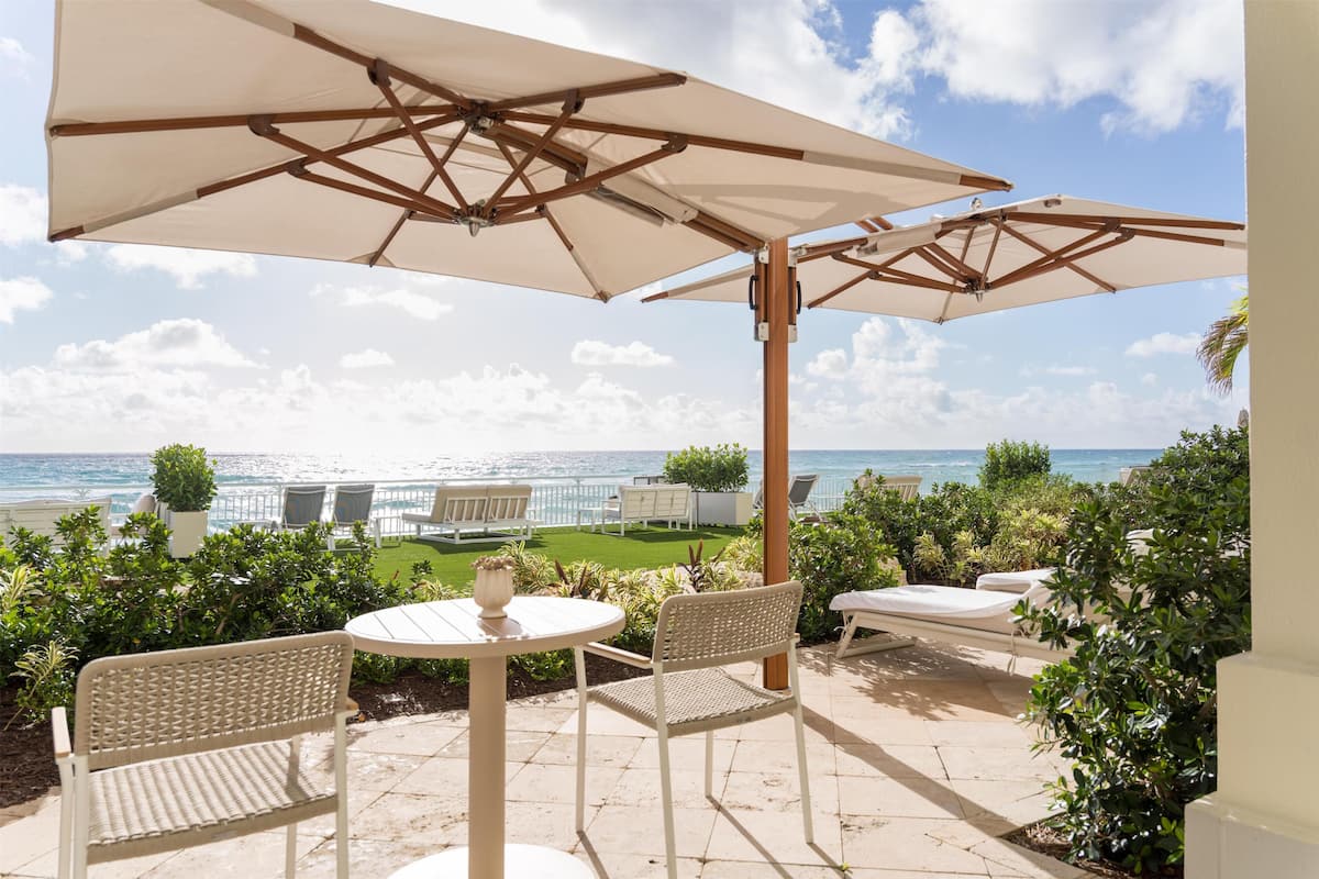 Een terras buiten met uitzicht op de oceaan, met een tafel, stoelen en parasols.