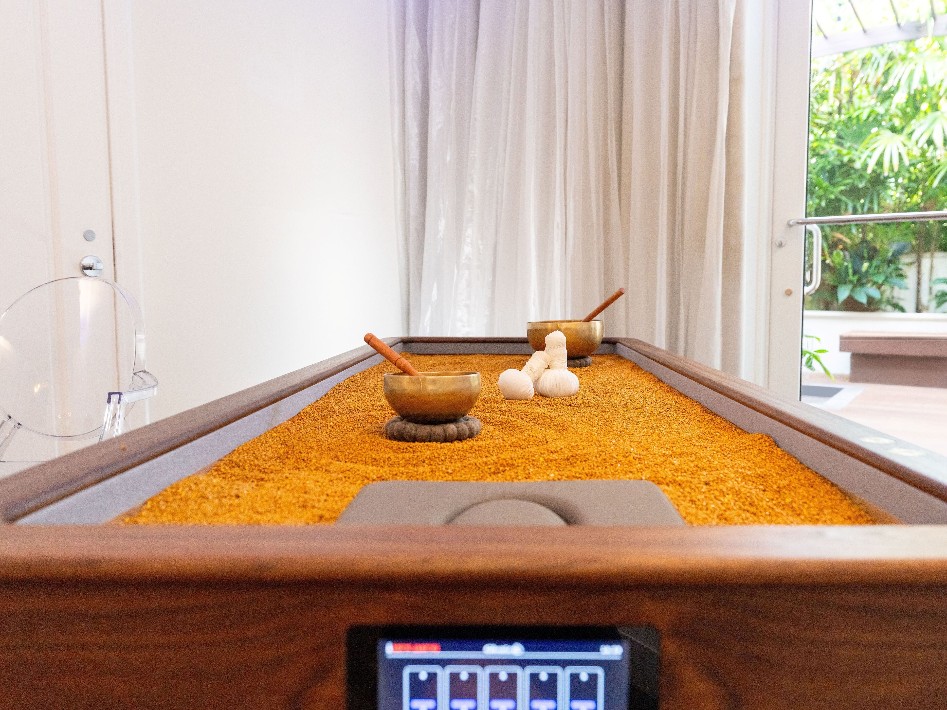A massage therapy room with a wooden table, two massage bowls, and a massage stone.