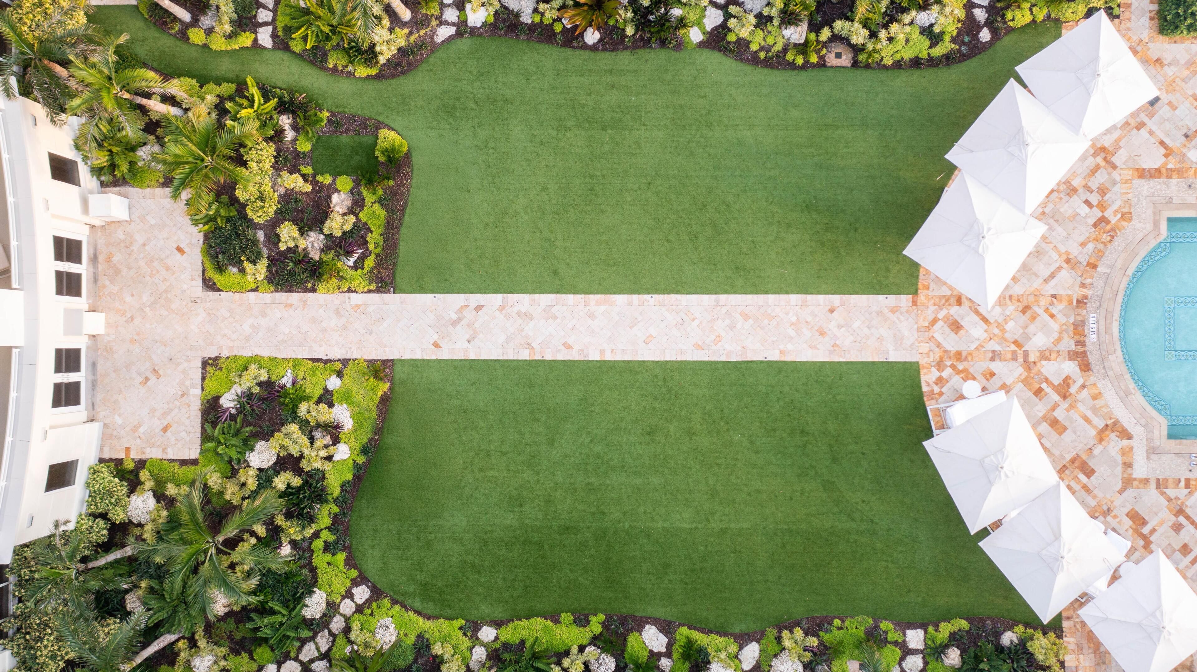 Luchtbeeld van een aangelegde binnenplaats met een grasveld in het midden, omringd door diverse planten en een zwembadgedeelte met parasols.